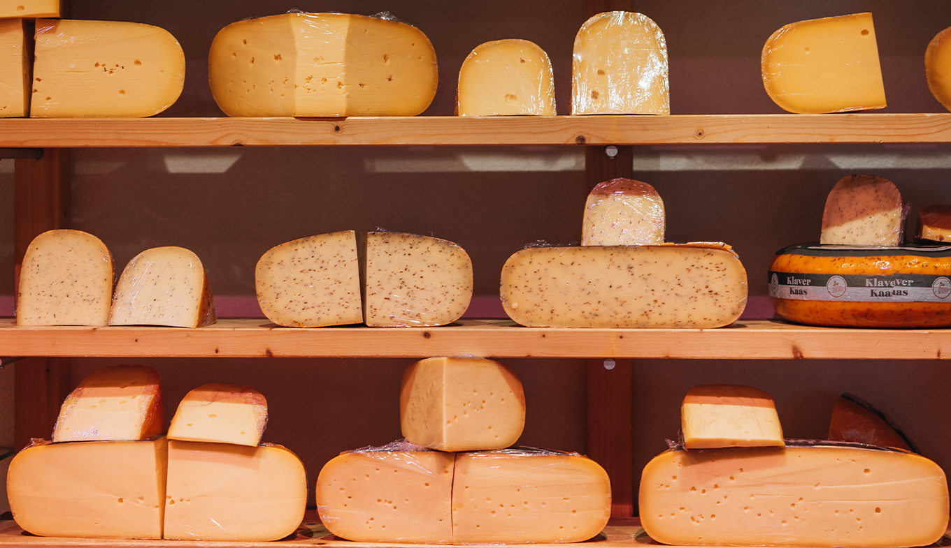 Assorted cheese wheels on shelves, with hues from light yellow to orange. Assorted cheese wheels on shelves, with hues from light yellow to orange.